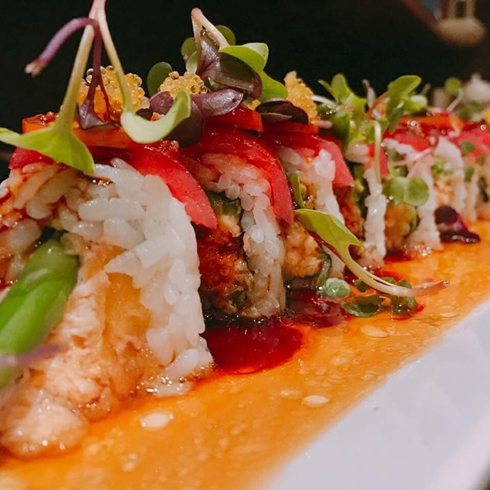 Sushi rolls with red tuna, green asparagus, and microgreens, drizzled with sauce on a white plate.